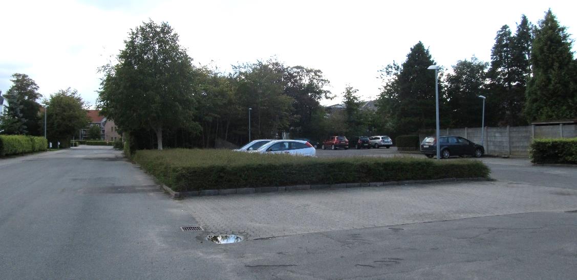Skolegades sydvestside er domineret af parkeringsområder. På billedet ses et bunkers-anlægget med tæt beplantning bag de to hvide biler.